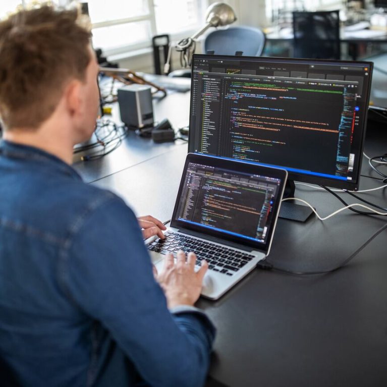 A_software_engineer_programming_with_laptop_and_computer-min